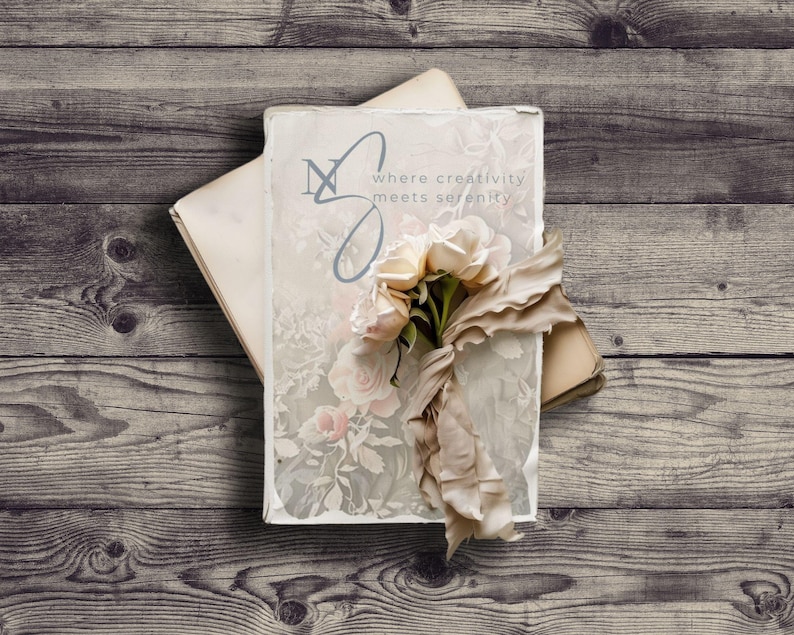 May include: A vintage book with a floral design and the text "where creativity meets serenity" on the cover. A bouquet of white flowers is placed on top of the book.