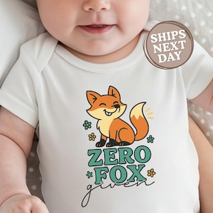 May include: White baby bodysuit with a smiling cartoon fox in orange and yellow, surrounded by green flowers. The text "ZERO FOX given" is below the fox. The brand logo is in the upper left corner.