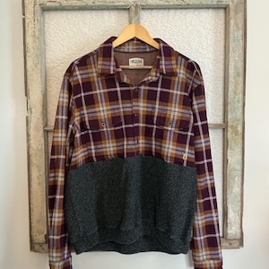 May include: A long-sleeved shirt with a plaid pattern in shades of burgundy, gold, and white, paired with a dark gray knit bottom. The shirt is hanging on a wooden hanger. The label reads "LAKE & TRAIL".