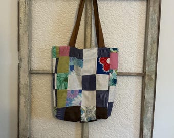 Könnte beinhalten: Eine Patchwork-Tragetasche mit braunen Henkeln hängt vor einem Vintage-Fensterrahmen. Die Tasche besteht aus verschiedenen Stoffquadraten in Farben wie Blau, Rosa, Grün und Weiß. Der Fensterrahmen ist verwittert mit einem cremefarbenen Finish.