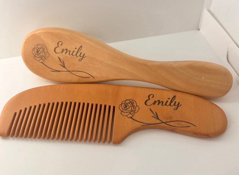 May include: A wooden hairbrush and comb set with the name "Emily" engraved on each piece. Both pieces feature a rose design.