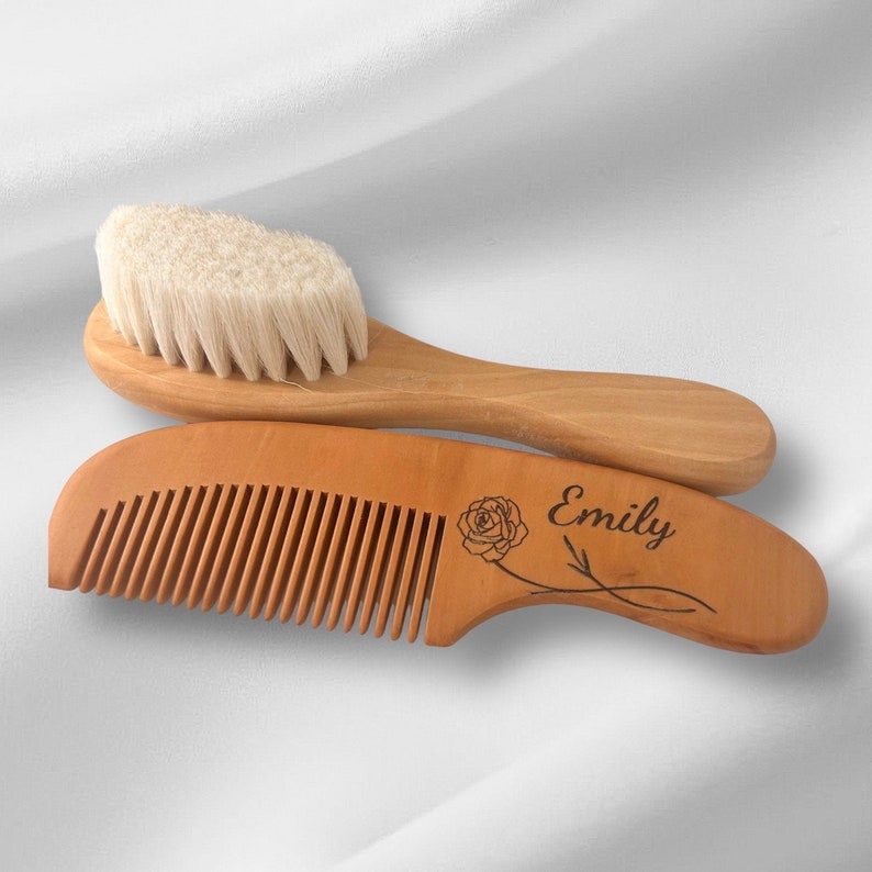 May include: A wooden baby hair brush and comb set with a personalized name "Emily" engraved on the comb handle. The comb has a rose design and the brush has natural bristles.