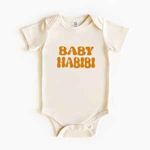 May include: A cream-coloured baby onesie with short sleeves and a brown retro-style font that reads "BABY HABIBI".