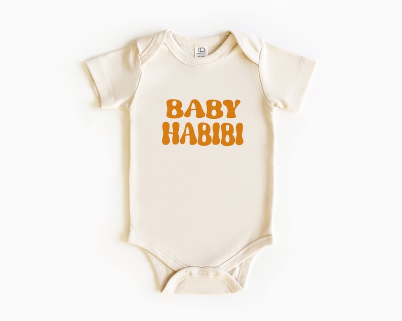 May include: A cream-coloured baby onesie with short sleeves and a brown retro-style font that reads "BABY HABIBI".