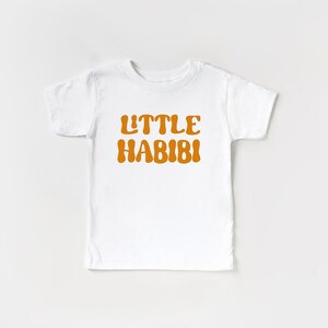 May include: White short-sleeved t-shirt with the text "LITTLE HABIBI" in orange.