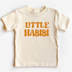 May include: A cream coloured short-sleeved t-shirt with the text "LITTLE HABIBI" in orange.