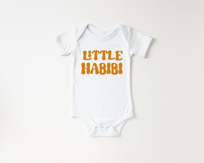 May include: White baby onesie with short sleeves and a brown text graphic that says "LITTLE HABIBI".