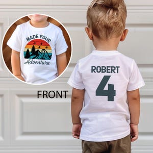 Peut inclure: T-shirt blanc avec un motif de montagne et de coucher de soleil avec l'inscription "MADE FOUR Adventure". Le dos du t-shirt affiche le nom "ROBERT" et le chiffre "4" en gris foncé.