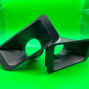 May include: Two black plastic vent covers with a round opening in the center. The vent covers are angled and have a smooth, matte finish.