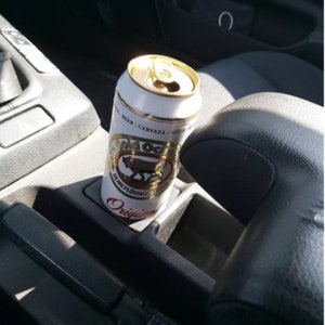 May include: A silver can of Old  Original beer in a car cup holder. The can has a gold bull logo and the text "Old Original" and "Bier, Cerveza, Biere".