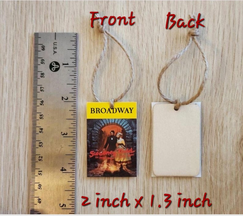 May include: A bookmark featuring a yellow and red image of the Broadway musical "Sweeney Todd: The Demon Barber of Fleet Street". The bookmark is 2 inches by 1.3 inches and has a brown twine string.