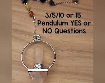 May include: A pink crystal pendulum with a silver chain and ring. The pendulum is hanging from a wooden surface. The text "3/5/10 or 15 Pendulum YES or NO Questions" is written on the surface.