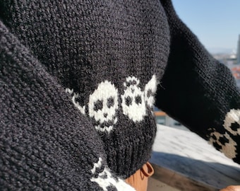 May include: Black knitted sweater with white skull designs. The sweater has long sleeves and a cropped length.