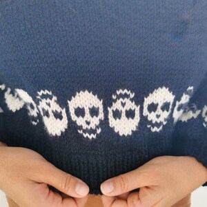K&ouml;nnte beinhalten: Ein dunkelblauer Strickpullover mit einem wei&szlig;en Totenkopf-Muster am unteren Saum.
