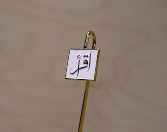 May include: A gold bookmark with a white rectangular tag that says "القدر" in Arabic calligraphy.