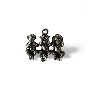 May include: A silver-toned charm featuring three monkeys in the 'see no evil, hear no evil, speak no evil' pose. Each monkey is in a seated position, with one covering its eyes, one its ears, and one its mouth.