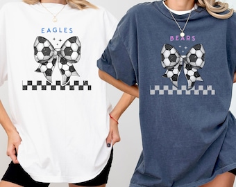 Könnte beinhalten: Zwei Frauen tragen übergroße T-Shirts mit einem Fußball-Schleifendesign. Das weiße Shirt sagt "EAGLES" und das blaue Shirt sagt "BEARS". Beide Shirts haben ein kariertes Muster unter der Schleife.