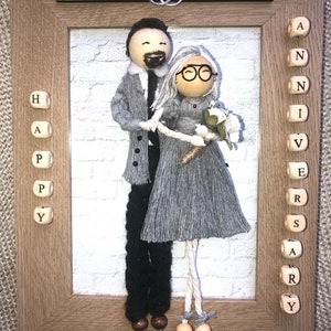 Könnte beinhalten: Ein Holzrahmen mit weißem Hintergrund und einem Paarporträt aus Garn. Das Paar hält einen Blumenstrauß. Der Rahmen hat eine Holzplakette oben mit den Namen "Melissa" und "John" und eine Plakette unten mit dem Datum "September 16, 1990". Der Rahmen hat auch Holzblöcke, die "Happy Anniversary" buchstabieren.