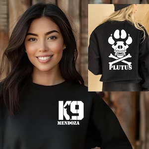 May include: Black sweatshirt with a white K9 logo and the text "MENDOZA" on the front. The back of the sweatshirt features a white skull and paw print with crossed bones and the text "PLUTUS".