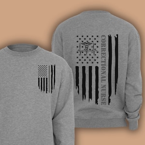 May include: A grey sweatshirt with a distressed American flag design on the left chest and a larger distressed American flag design on the back with the text "Correctional Nurse" on the right side of the flag.