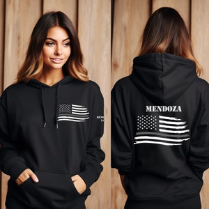 May include: Black hooded sweatshirt with a white American flag with a thin gray line across it. The back of the sweatshirt has the name "MENDOZA" printed above the flag.