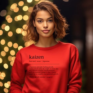 May include: A woman wearing a red sweatshirt with the word "kaizen" and its definition printed on the front. The definition explains that kaizen is a Japanese principle that encourages continuous improvement.