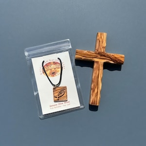 May include: A wooden cross and a square pendant necklace on a display card inside a clear plastic sleeve. The pendant features a fish symbol with the word JESUS engraved. The card text reads Bethlehem Nativity Star and Genuine Olive Wood.