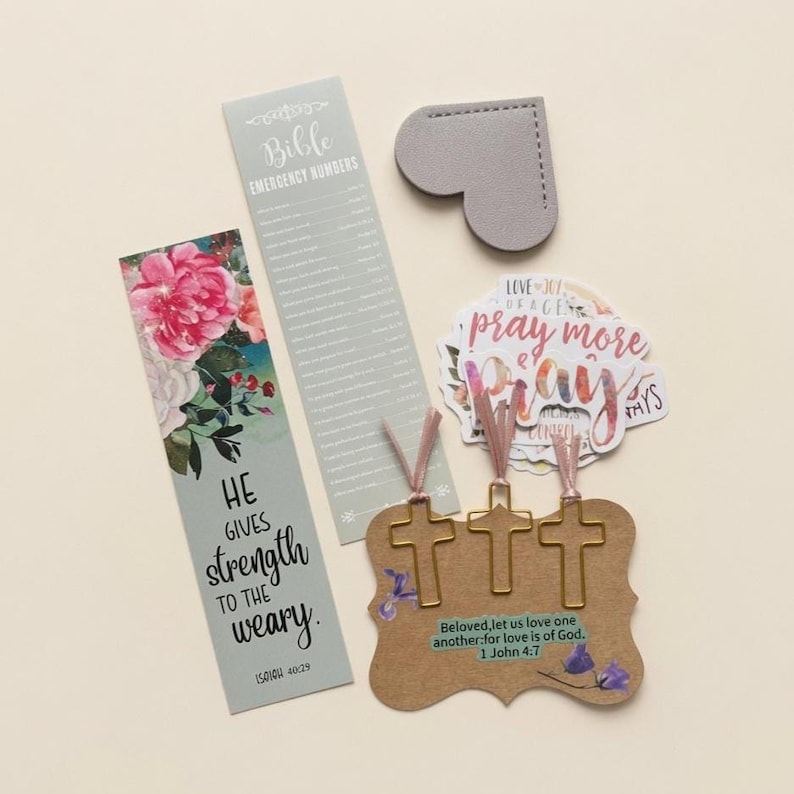 May include: A collection of religious stationery including a bookmark with floral art and the text He gives strength to the weary, a Bible emergency numbers list, a gray heart-shaped tag, stickers with the text Pray more, and three cross paperclips.