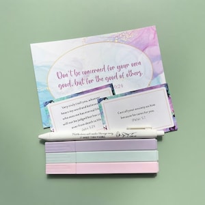 May include: A set of three pastel-colored pens in lavender, mint, and light pink, accompanied by two small rectangular cards and one larger rectangular card featuring watercolor backgrounds and printed religious scripture text.