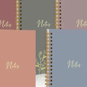 May include: A collection of five spiral-bound notebooks in muted shades of dusty rose, dark gray, mauve, light peach, and slate blue. Each notebook features a gold-colored metal wire binding and the word Notes written in gold cursive script on the cover.