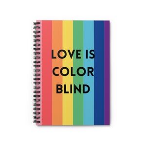 May include: A spiral bound notebook with a rainbow striped cover and the text "LOVE IS COLOR BLIND" in black.