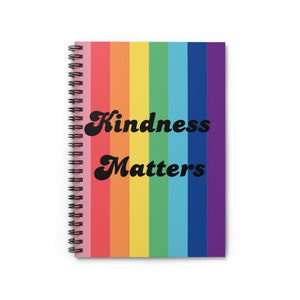以下が含まれることがあります： 虹色のストライプの表紙と「Kindness Matters」という黒いテキストが書かれた、スパイラルバインディングされたノートブックです。