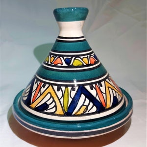 May include: A teal and white ceramic tagine pot with a conical lid. The lid features a geometric pattern in orange, yellow, and blue. The base has a circular design with teal and white stripes. This decorative cookware is suitable for cooking and serving.