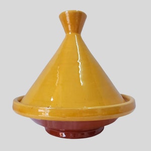 Puede incluir: Una tagine de cerámica amarilla con una tapa cónica y una base ancha y redonda. La base es de un tono marrón más oscuro.