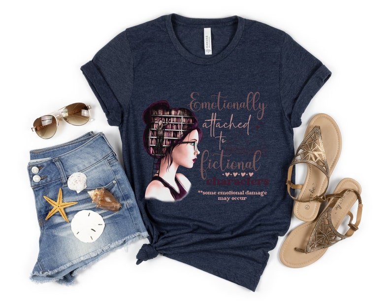 May include: A navy blue t-shirt with a graphic of a woman with books stacked on her head. The text on the shirt reads "Emotionally attached to fictional characters" with the words "some emotional damage may occur" below.