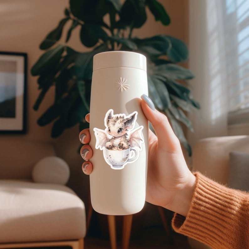 May include: White ceramic water bottle with a sticker of a small, brown and white dragon sitting in a teacup. The dragon has wings and a cute face.