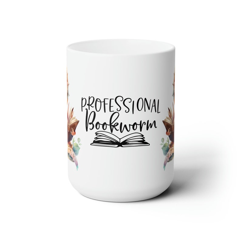 Op de afbeelding: Witte keramische mok met een zwart-wit ontwerp van een open boek en de tekst "PROFESSIONAL BOOKWORM". Het ontwerp is omgeven door aquarel-achtige bloemelementen in tinten bruin, roze en groen.