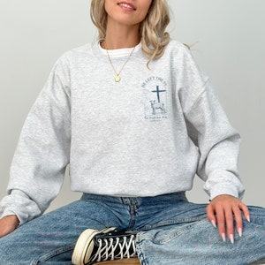 Pu&ograve; includere: Una felpa grigia con una stampa grafica di una croce e un cervo. Il testo sulla grafica recita "He left the 99 to rescue me Luke 19:10".