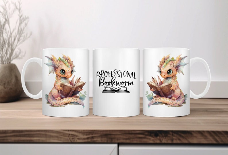 Op de afbeelding: Drie witte keramische mokken met een drakenontwerp. De mokken links en rechts hebben een klein, oranje draakje dat een boek leest. De mok in het midden heeft de tekst "Professional Bookworm" met een stapel boeken eronder.