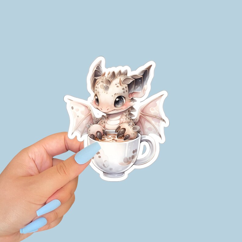 May include: A white and brown dragon with wings sits in a white teacup with a brown liquid inside. The dragon has a light pink nose and light blue eyes.
