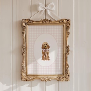 May include: A framed print with a watercolour illustration of a brown poodle wearing a pink bow. The print is set against a pink and white gingham background within an ornate gold frame, suspended by a white ribbon.