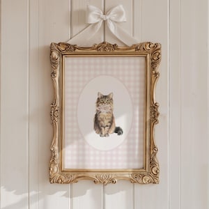 Puede incluir: Una impresión enmarcada de un gato marrón y blanco con una pajarita rosa. La impresión está sobre un fondo de cuadros vichy rosa y blanco.