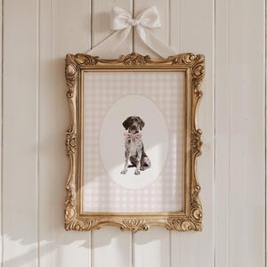 以下が含まれることがあります： ピンクのリボンタイをした犬の額縁入りプリント。プリントはピンクと白のギンガムチェックの背景にあり、金色の装飾的なフレームに入っています。