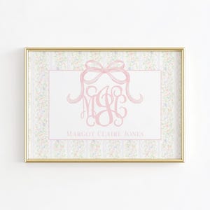 May include: A framed print featuring a pink monogram and bow design. The print includes the name "Margot Claire Jones" in a delicate script. The background has a floral pattern in soft pastel colors, framed in a gold border.