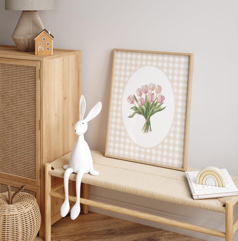Pu&ograve; includere: Una stampa incorniciata di un mazzo di tulipani rosa con foglie verdi su uno sfondo a quadri vichy beige e bianco. La stampa &egrave; in una cornice di legno ed &egrave; appesa a un muro bianco.