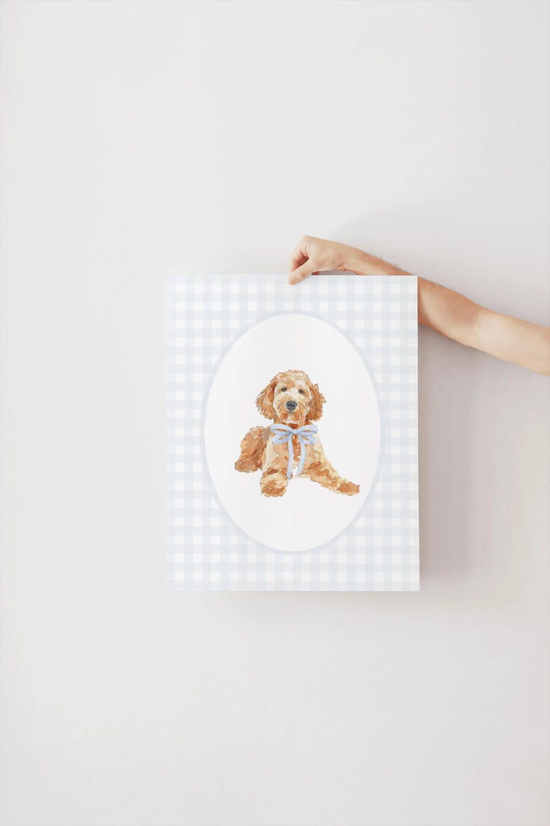 Pode incluir: Impress&atilde;o em aquarela de um c&atilde;o golden doodle com um la&ccedil;o azul, inserida em um oval sobre um fundo xadrez azul claro e branco. A obra de arte &eacute; segurada por uma m&atilde;o.
