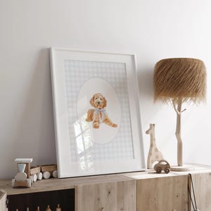 Pode incluir: Uma impress&atilde;o em aquarela emoldurada de um c&atilde;o golden doodle com um la&ccedil;o azul, em um fundo xadrez cinza e branco. A moldura branca &eacute; exibida em um arm&aacute;rio de madeira, junto com um trem de madeira, uma girafa e um carro.