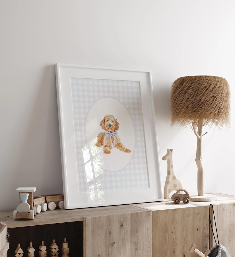 Pode incluir: Uma impress&atilde;o em aquarela emoldurada de um c&atilde;o golden doodle com um la&ccedil;o azul, em um fundo xadrez cinza e branco. A moldura branca &eacute; exibida em um arm&aacute;rio de madeira, junto com um trem de madeira, uma girafa e um carro.