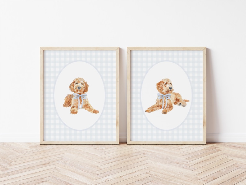 May include: Two framed prints with watercolour illustrations of a golden doodle dog. Each dog is lying down with a light blue bow. The background is a light blue and white checkered pattern.