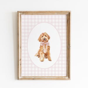 May include: A framed print of a watercolor painting of a golden doodle dog wearing a pink bow, set against a pink and white gingham background.